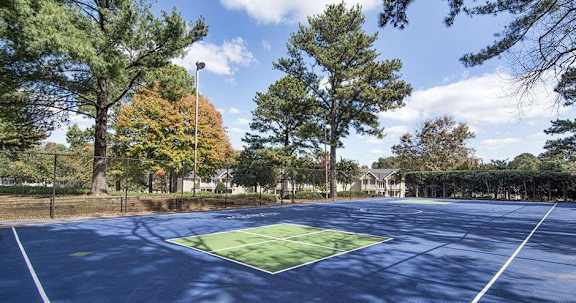A tennis court surrounded by trees and a fence.