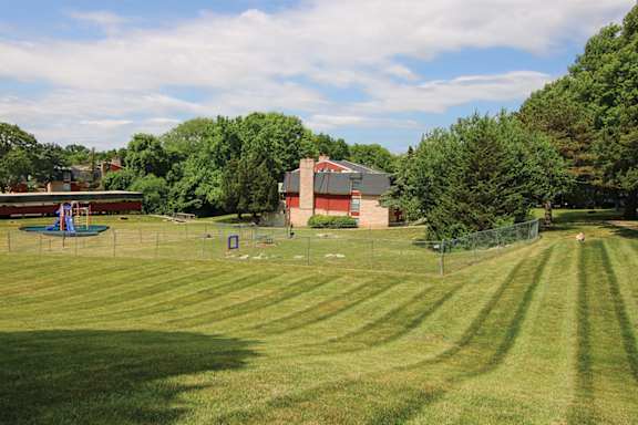 A grassy field with a building and trees in the background.