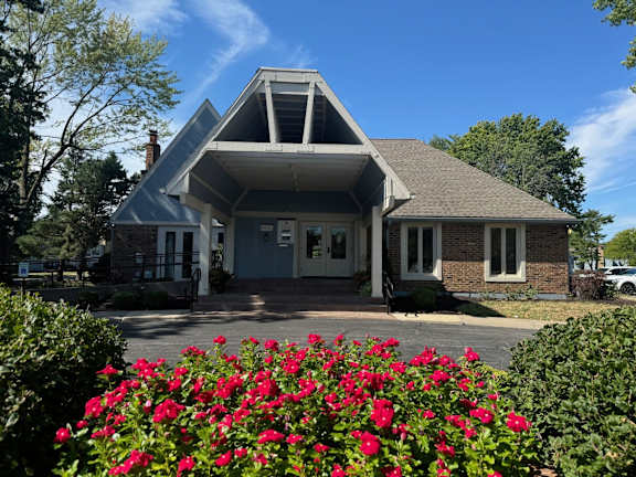 A house with a white front porch and a large bush of red flowers in front.