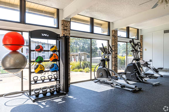 A gym with a variety of exercise equipment including a weight rack with dumbbells and a rowing machine.