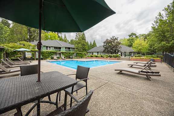 A pool area with a table and chairs and a green umbrella.
