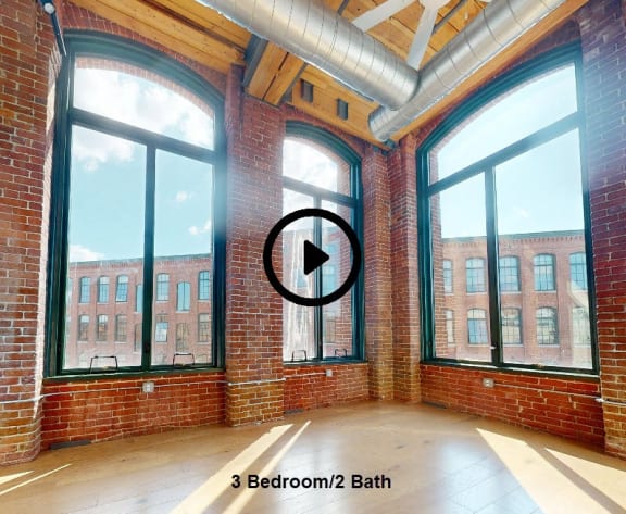 a living room with three large windows and a brick wall