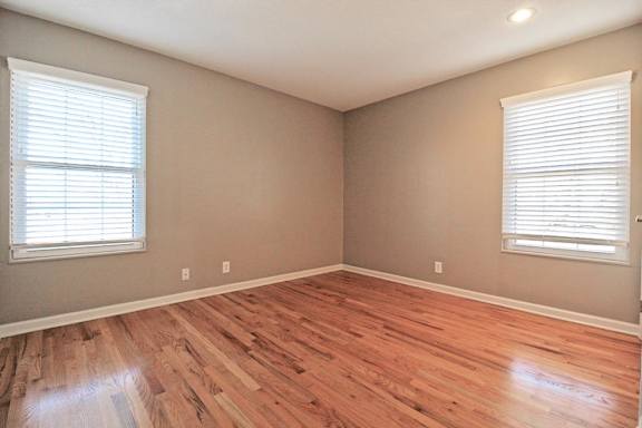 A room with wooden floors and two windows with blinds.