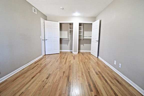 A room with wooden floors and white walls with two open closets.