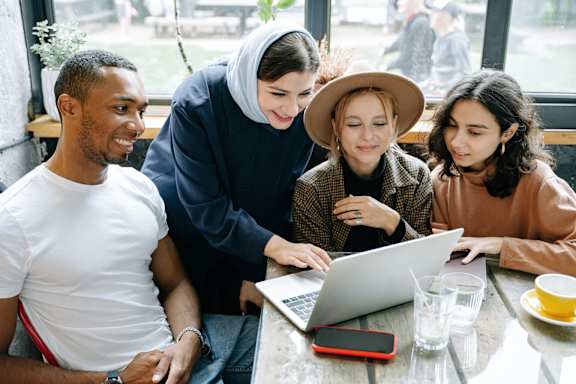 Four people are gathered around a laptop in a cafe.