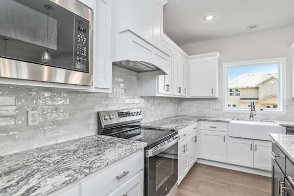 A kitchen with white cabinets and a marble countertop.