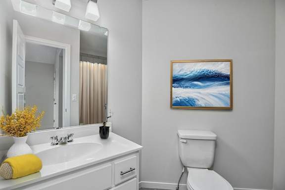 A bathroom with a white toilet and a painting of a wave on the wall.