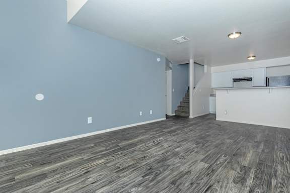 A room with wooden flooring and a staircase in the background.