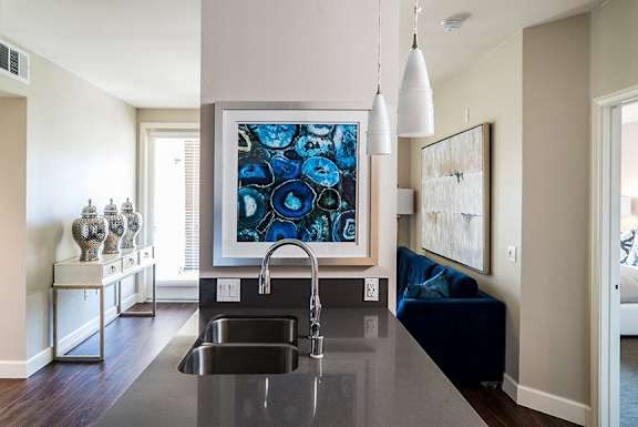 A kitchen with a black counter top and a large blue and black painting above the sink.