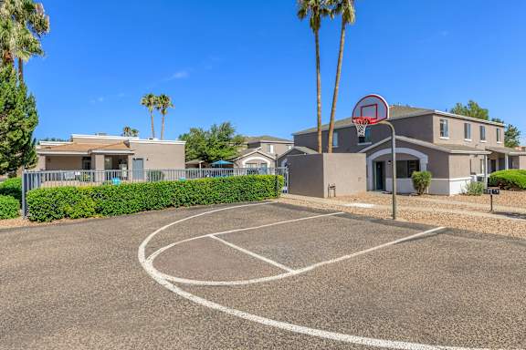 A basketball court is located in front of a building with a basketball hoop mounted on it.