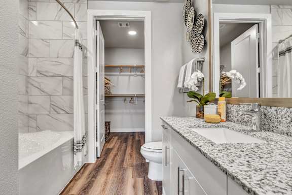 A bathroom with a marble patterned sink and wooden floors.