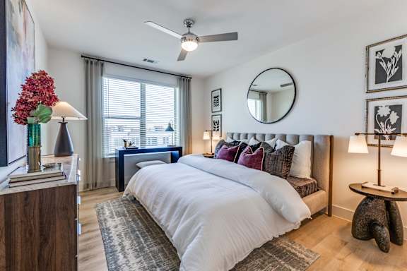 A bedroom with a large bed, a ceiling fan, and a mirror on the wall.