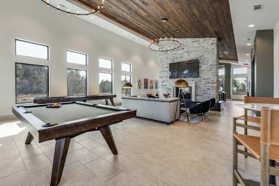 A billiard table is in the middle of a room with a stone fireplace and a TV above it.