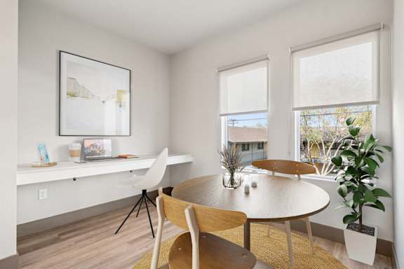 A white desk with a laptop and a white chair in a room with a window.