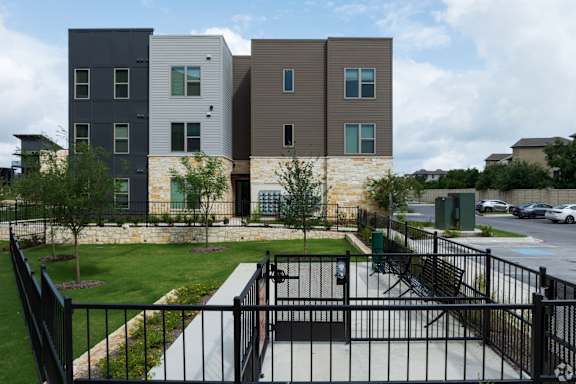 A black metal fence surrounds a small park area in front of a modern apartment building.