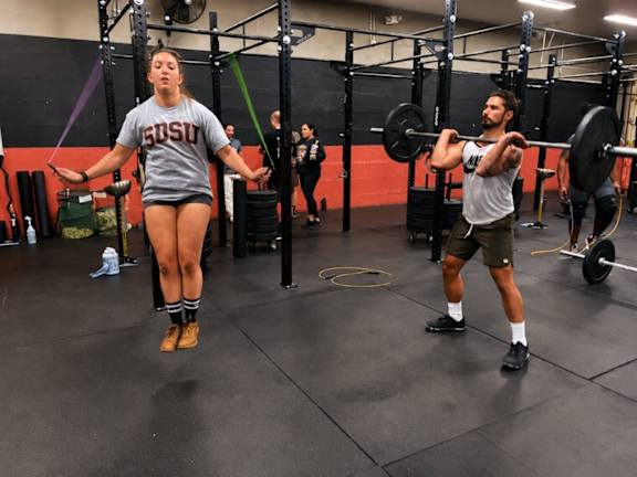 A woman in a SOSU shirt is doing a box jump in a gym.