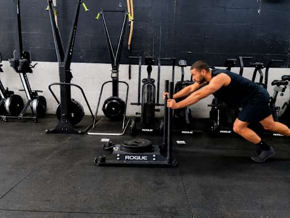 A man is working out on a Rogue exercise machine in a gym.