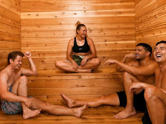 Four people relaxing in a wooden sauna.