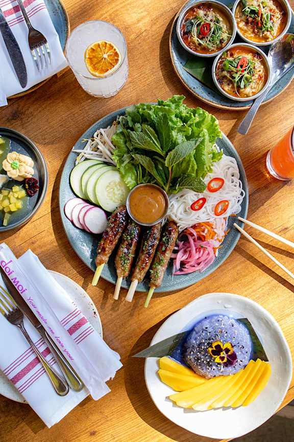 A table full of different foods including a plate of sushi and a plate of fruit.