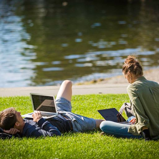 two people laying on the grass with laptops