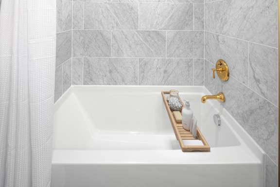 A white bathtub with a gold faucet and a tray with toiletries on it.