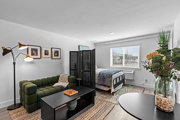 A modern living room with a dark green sofa, a black coffee table, and a large window with white blinds.