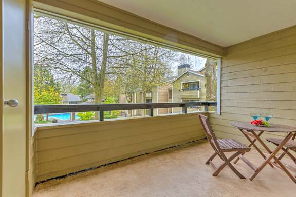 A balcony with a table and chairs overlooking a pool and trees.