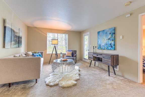 A living room with a beige couch, a glass table, and a painting on the wall.