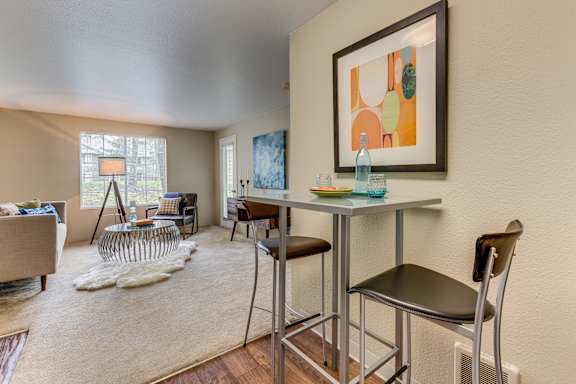 A living room with a grey sofa, a white rug, a glass table and a painting on the wall.