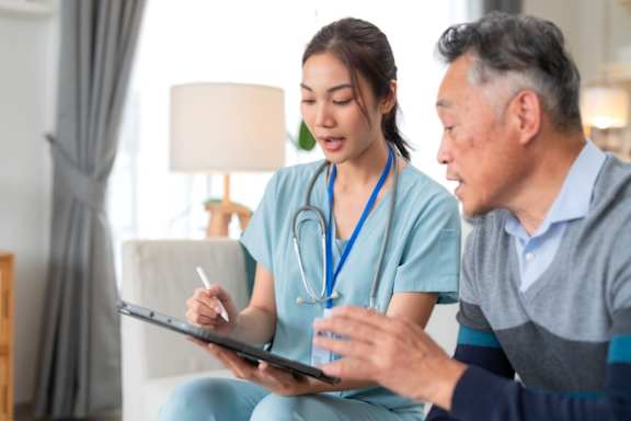 A healthcare professional is taking notes on a clipboard while consulting with a patient.