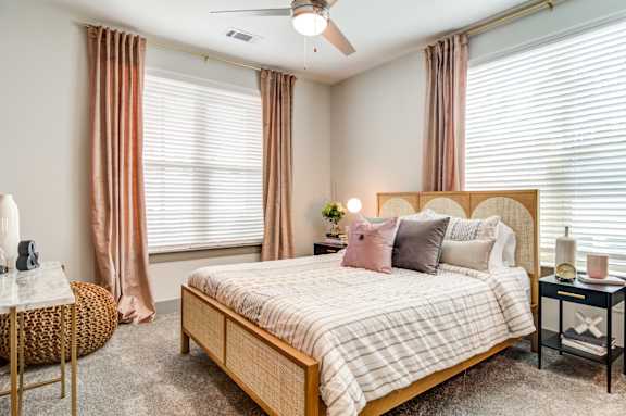 A bedroom with a large bed, a round wicker table, and a ceiling fan.