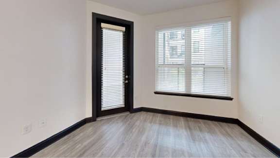 A room with a wooden floor and a window with blinds.