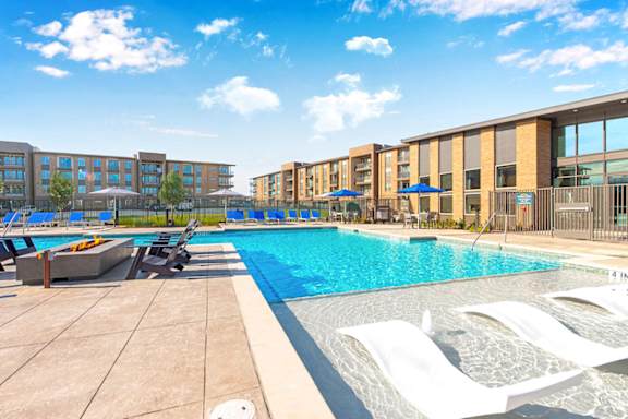 A swimming pool with sun loungers and apartment buildings in the background.