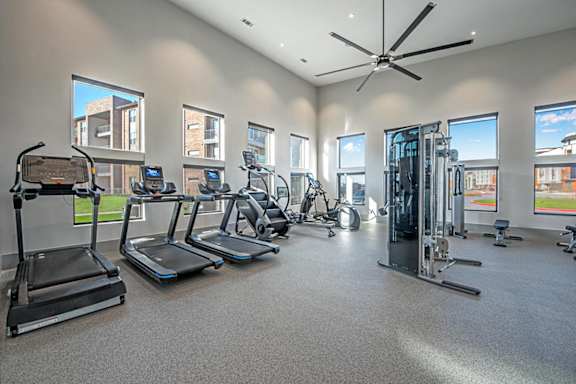 A spacious gym with treadmills, elliptical machines, and a fan.
