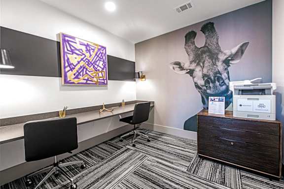 A room with a giraffe mural on the wall and a black chair in front of a desk.