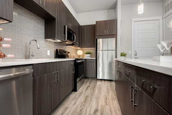 A modern kitchen with dark wood cabinets and stainless steel appliances.