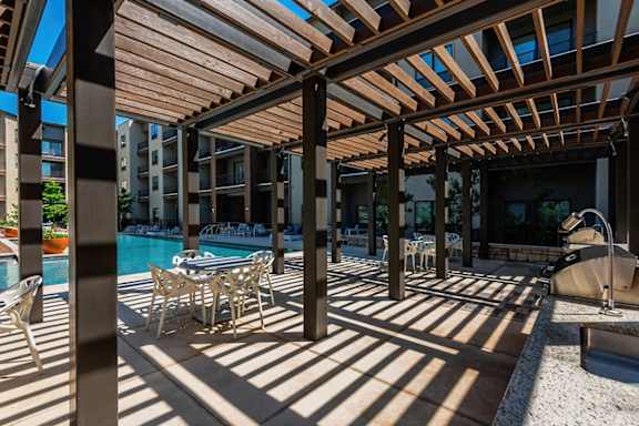 A wooden pergola shades a poolside table.