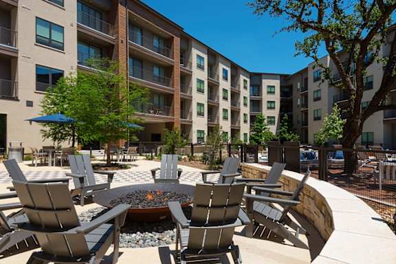 A patio with chairs and a fire pit in front of apartment buildings.
