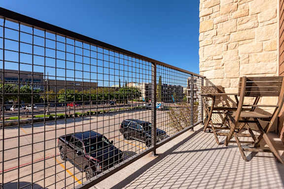 A black car is parked behind a metal fence on a sunny day.