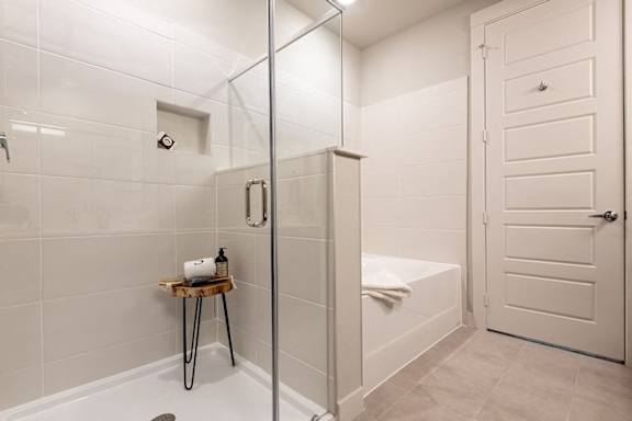 A white bathroom with a glass shower door and a white towel on the bathtub.