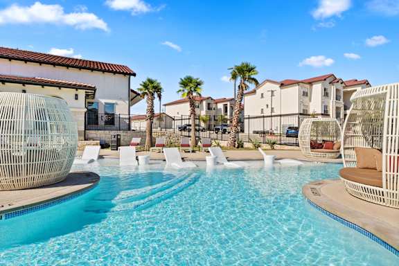 A pool with a blue tinted water and white chairs around it.