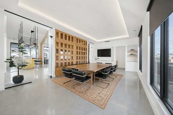 A modern living room with a large wooden table and black chairs.