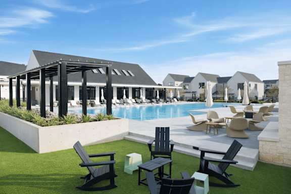 A poolside area with black chairs and a white building in the background.