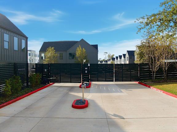 A concrete driveway leads to a black fence and a grey house.