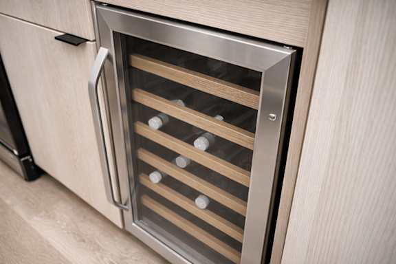 A stainless steel wine cooler is built into a wooden cabinet.