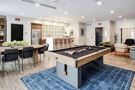 A pool table is in the middle of a room with a bar and chairs.