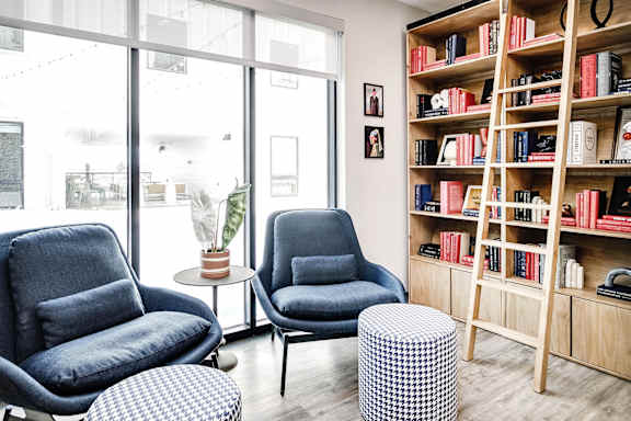 Two blue chairs and a table in a room with a bookshelf.