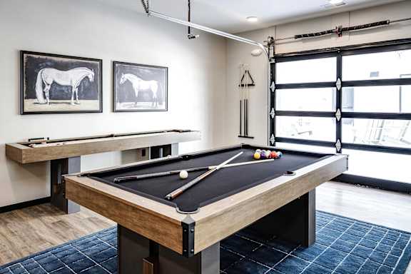 A pool table in a room with two framed horse pictures on the wall.