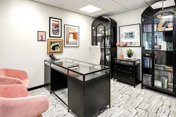 A black and white office with a glass desk and a pink chair.