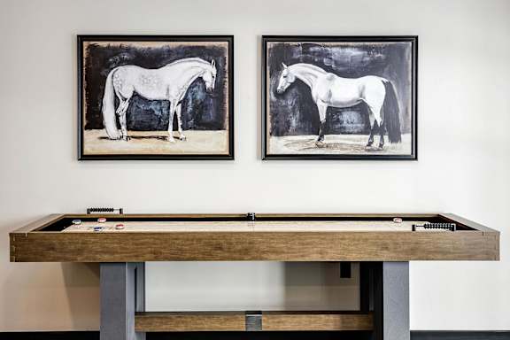 Two framed black and white horse paintings hang on a wall above a pool table.